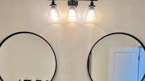 A bathroom with two round mirrors, a granite countertop, a black basket with a plant, and a white door in the background.