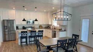 A modern kitchen with white cabinets, stainless steel appliances, and a dining area with a wooden table and chairs. - The Lyman House (Lyman)