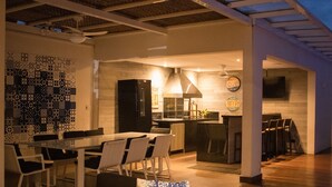 A modern kitchen with a built-in oven, a dining area with a glass table and chairs, and a bar area with stools. - Casa 5 Estrelas Top!!! All Incluse com 3 Funcionários (Praia de Maresias São Sebastião)