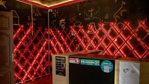 Una habitación con un separador iluminado con neón rojo, una puerta de madera y un tablón de anuncios con varias pegatinas y avisos.