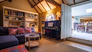 A cozy living room with a sofa, a coffee table, a bookshelf, and a piano. - 'Darling Buds of May' Glorious 17th Century Idyll (Heddington)