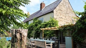 A stone house with a pitched roof, a patio with a table and chairs, and a pergola. - 'Darling Buds of May' Glorious 17th Century Idyll (Heddington)