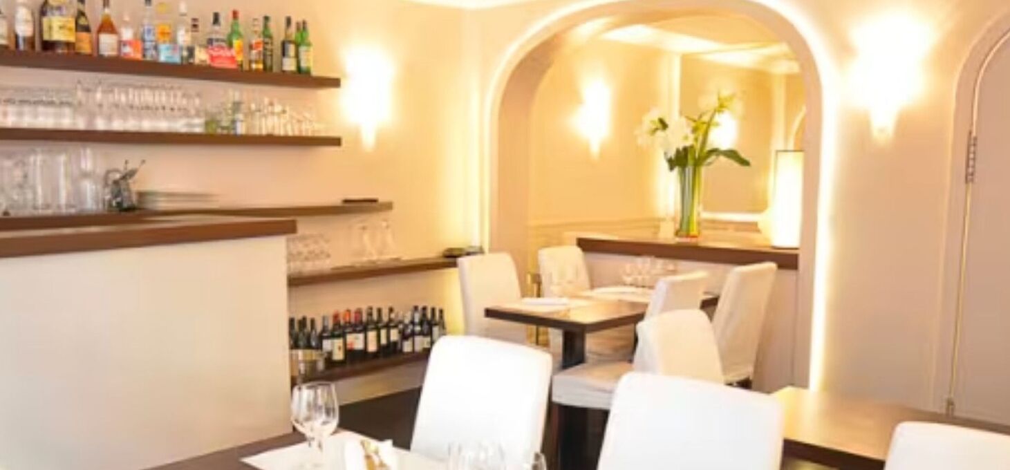 A restaurant with a bar area, white chairs, and a table set for dining.