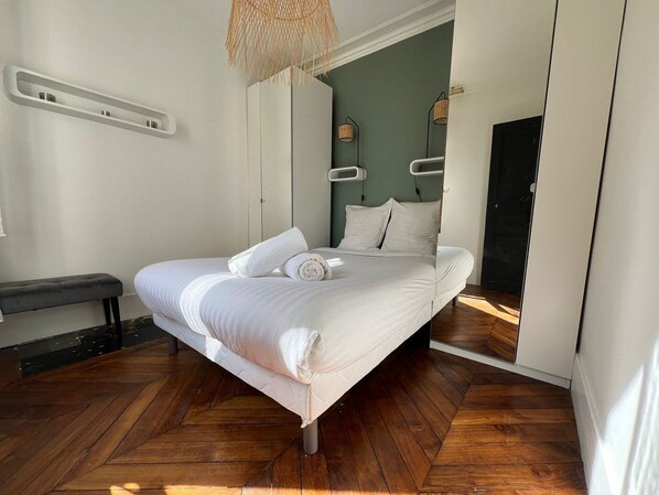 A modern bedroom with a large bed, wooden flooring, and a hanging light fixture.