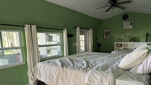 A bedroom with a large bed, a ceiling fan, a window with curtains, and a view of the outdoors. - Paradise Palms on Rainbow Ranch (Dunnellon)
