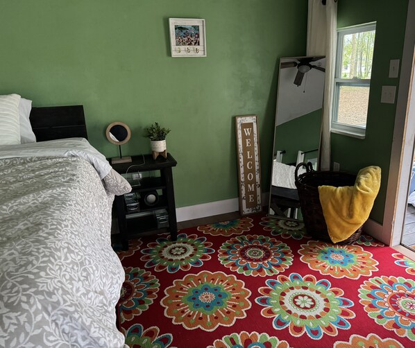 Une chambre à coucher comprenant un lit, une table de chevet, un miroir, une pancarte de bienvenue et une fenêtre donnant sur des arbres.