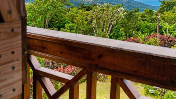 A wooden deck with a view of a lush landscape, including mountains and a body of water. - Roxy's Mountain Lodge (Laudat)