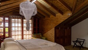 A bedroom with a wooden ceiling, a bed with white bedding, a window with curtains, and a chair. - Roxy's Mountain Lodge (Laudat)