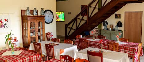 Comedor con varias mesas cubiertas de manteles a cuadros rojos y blancos, sillas de madera y una escalera de madera.