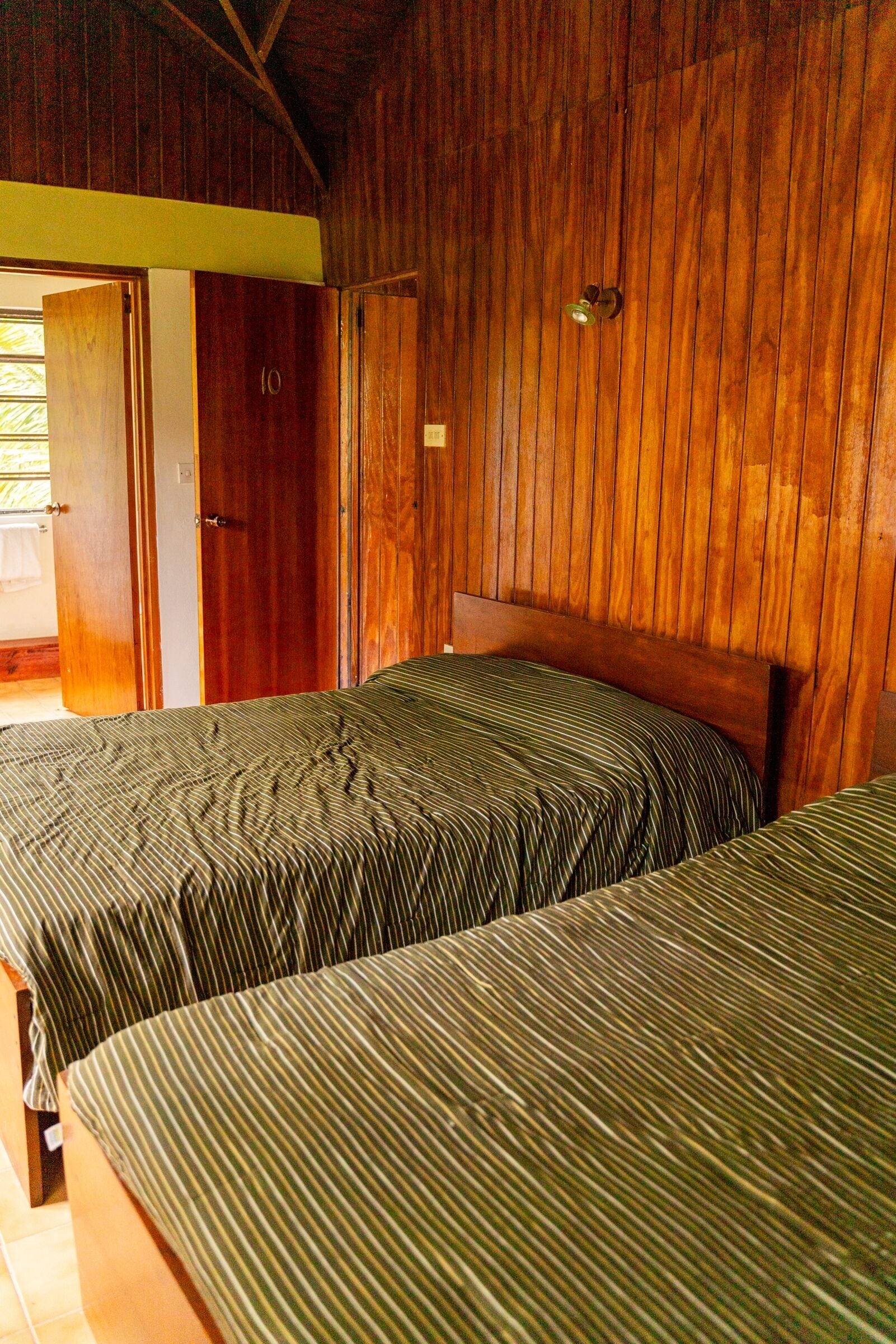 Una habitación con dos camas, paredes de madera y una puerta que da a otra estancia.