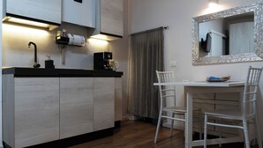 Une cuisine compacte équipée d’une cuisinière intégrée, d’une machine à café et d’un évier. Un coin repas est aménagé avec une table et des chaises blanches.