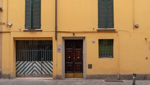 Un bâtiment jaune avec une porte en bois, des volets verts et une fenêtre grillagée.