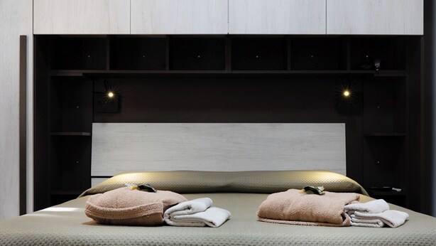 Une chambre moderne au design minimaliste, comprenant un lit doté d’un matelas texturé, de deux oreillers et d’une tête de lit pourvue d’un éclairage intégré.