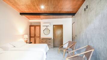 Ein Hotelzimmer mit zwei Betten, einer Holzbalkendecke, einer Wandklimaanlage und einer Tür zu einem anderen Raum.