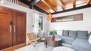 Uma sala de estar moderna com teto de madeira, um sofá cinza, uma mesa de centro redonda e uma cadeira de vime.