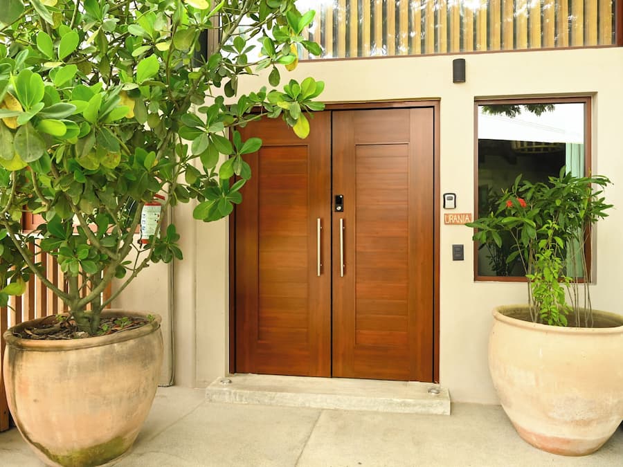 A wooden door with a sign reading "URANIA" and a large potted plant to the right.