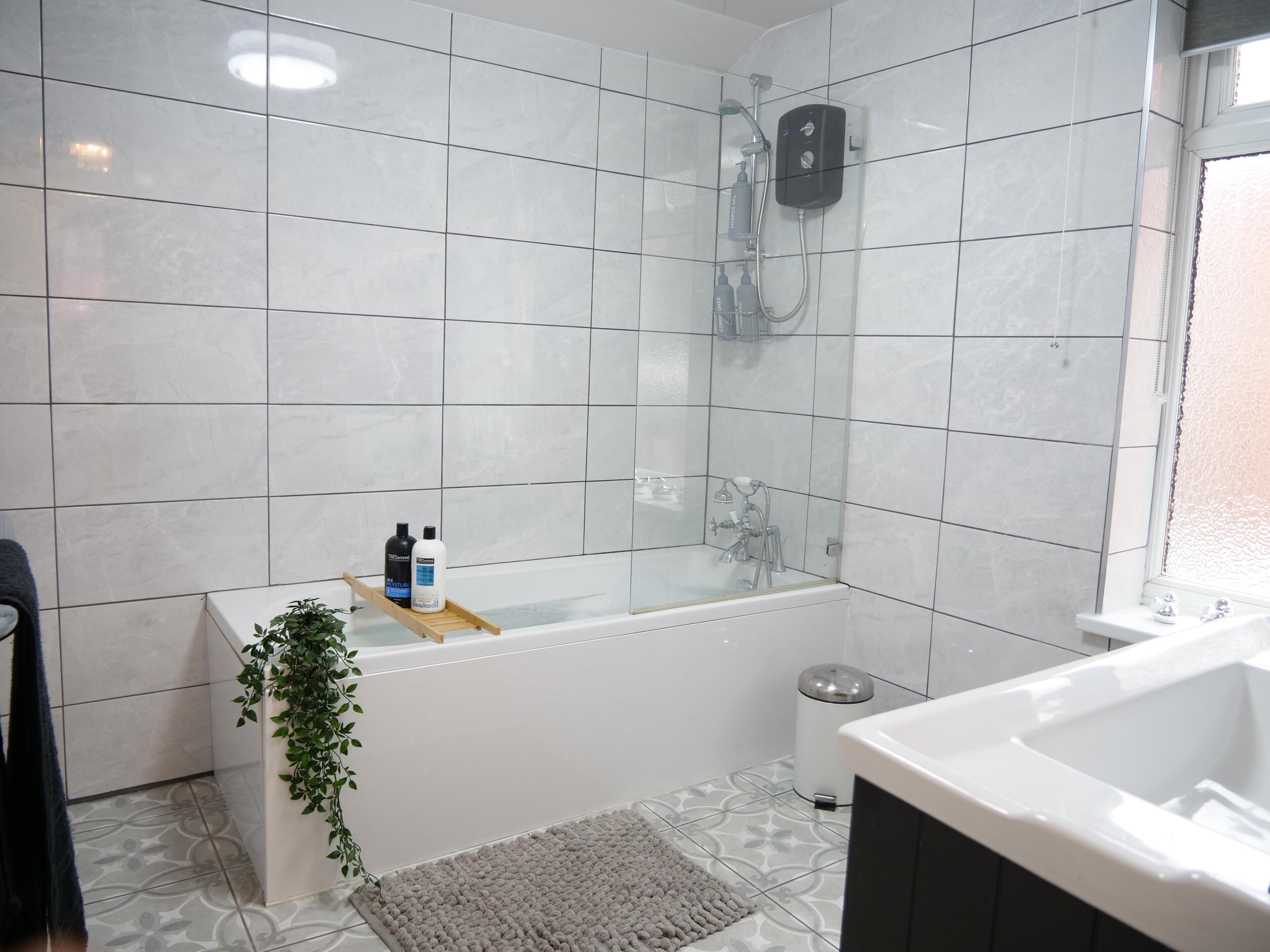 Un bagno con vasca, doccia e WC. Prodotti da bagno su uno scaffale e una pianta accanto alla vasca.