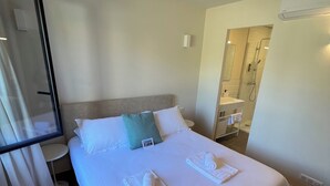 A hotel room with a bed, a bedside table, a mirror, and a bathroom visible through an open door. - Appartement 2 Chambres (Saint-Florent)