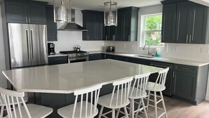 Cocina moderna con armarios oscuros, una isla grande con taburetes de bar, electrodomésticos de acero inoxidable e iluminación colgante.