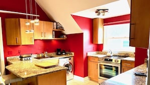A compact kitchen with a red wall, wooden cabinets, a built-in oven, a washing machine, and a coffee maker. - Large Luxury Downtown "Design Studio" One Bedroom Apartment (Findlay)