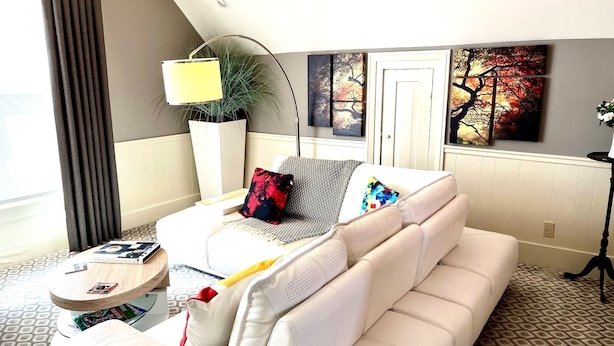 A modern hotel room with a white sofa, a round side table, a floor lamp, and artwork on the walls. - Large Luxury Downtown "Design Studio" One Bedroom Apartment (Findlay)