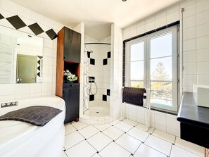 Enjoy a spacious bathroom with a large bathtub, walk-in shower, and window offering a view of the outdoors.