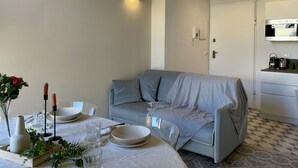 A modern dining area with a round table set for two, a grey sofa, and a white door in the background. - [villa Migliorini] Lusso & Comfort in Finalborgo (Finale Ligure)