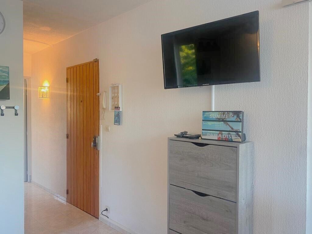 A hallway with a wooden door, a wall-mounted TV, and a small cabinet with a board game.