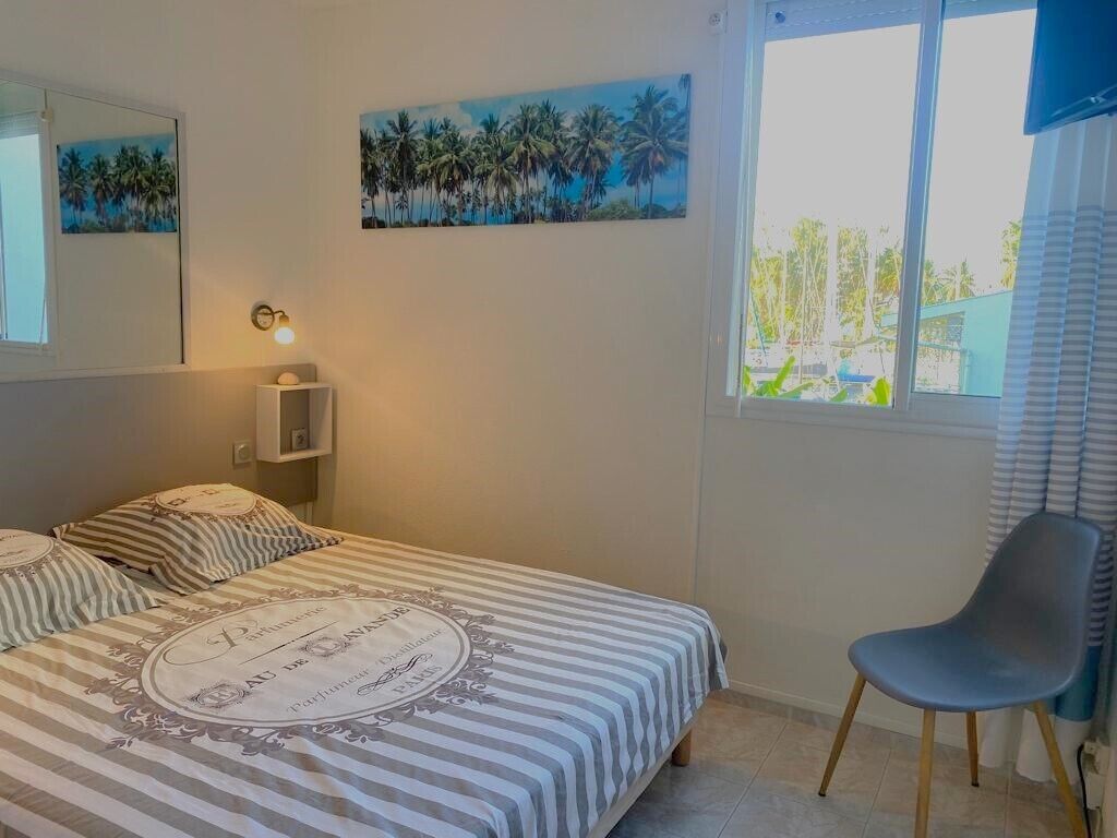A bedroom with a bed, a chair, a nightstand, a wall-mounted lamp, and two paintings.