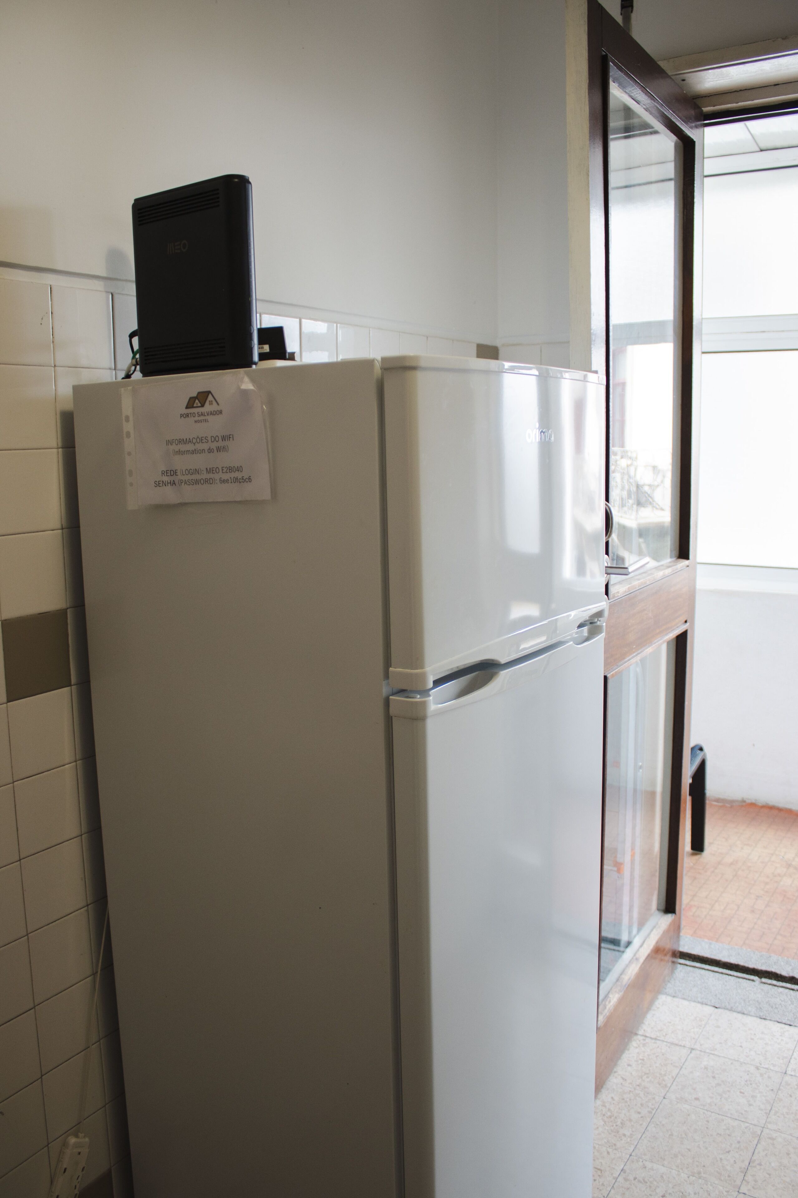 A white refrigerator with a black device on top, a glass door, and a sign with WiFi information.