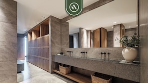 Een moderne badkamer met een grote spiegel, houten kastjes en een marmeren aanrechtblad.