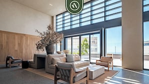 Een moderne lobby met een ruim zithoek, een potplant en grote ramen met uitzicht op de stad.