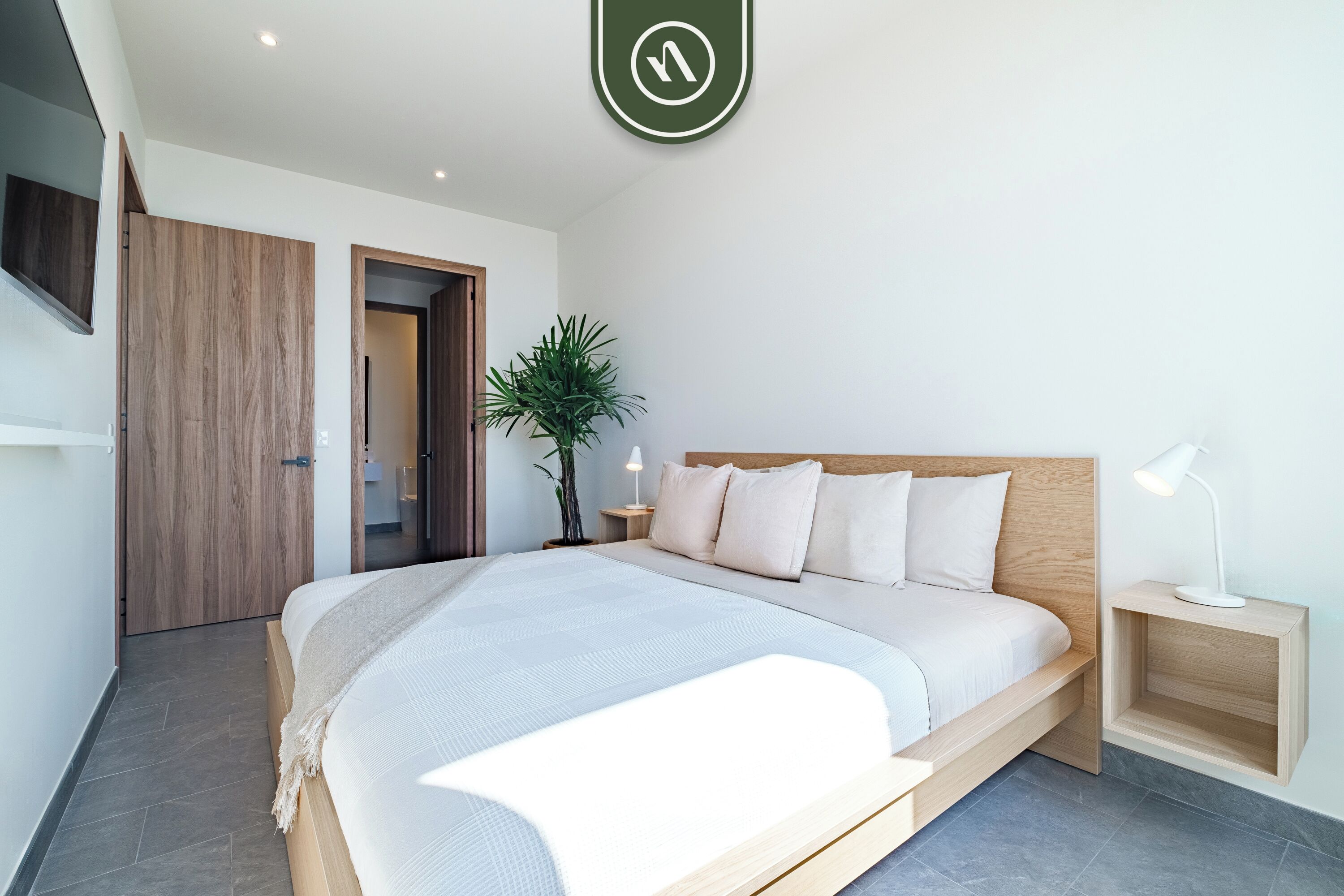 Ein modernes Schlafzimmer mit einem großen Bett, einem Holzkopfende, Nachttischen und einer Topfpflanze.