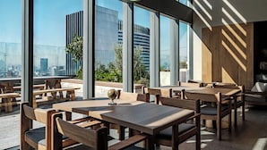 Een terras op het dak met houten tafels en stoelen, grote ramen met uitzicht over de stad.