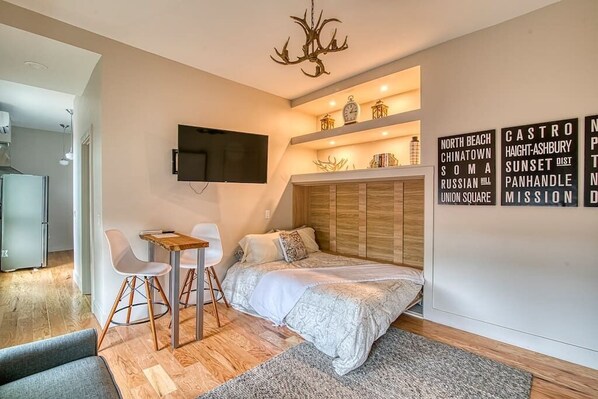 Une chambre à coucher moderne, avec un lit, un bureau et des chaises, un téléviseur fixé au mur et un lustre décoratif.