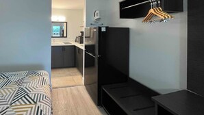 A compact room with a bed, a small kitchenette, a refrigerator, and a hanging clothes rack. - Studio 6 Conroe, TX (Conroe)