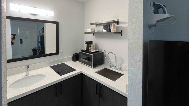A modern bathroom with a large mirror, a sink, a countertop with a coffee maker, and a shower area. - Studio 6 Conroe, TX (Conroe)
