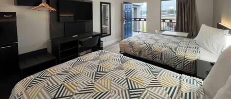 A hotel room with two beds, a desk with a chair, a TV mounted on the wall, and a balcony with a view.