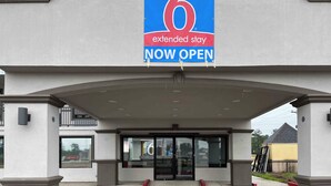 An extended stay hotel entrance with a large sign indicating it's now open. - Studio 6 Conroe, TX (Conroe)