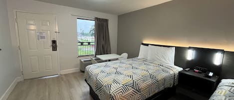 A hotel room with a bed, a desk, a chair, a window with curtains, and a door.