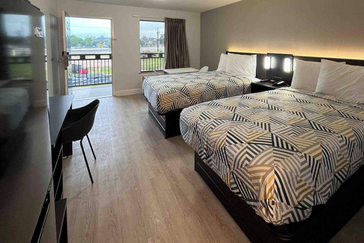 A hotel room with two beds, a desk, a chair, and a balcony with a view.