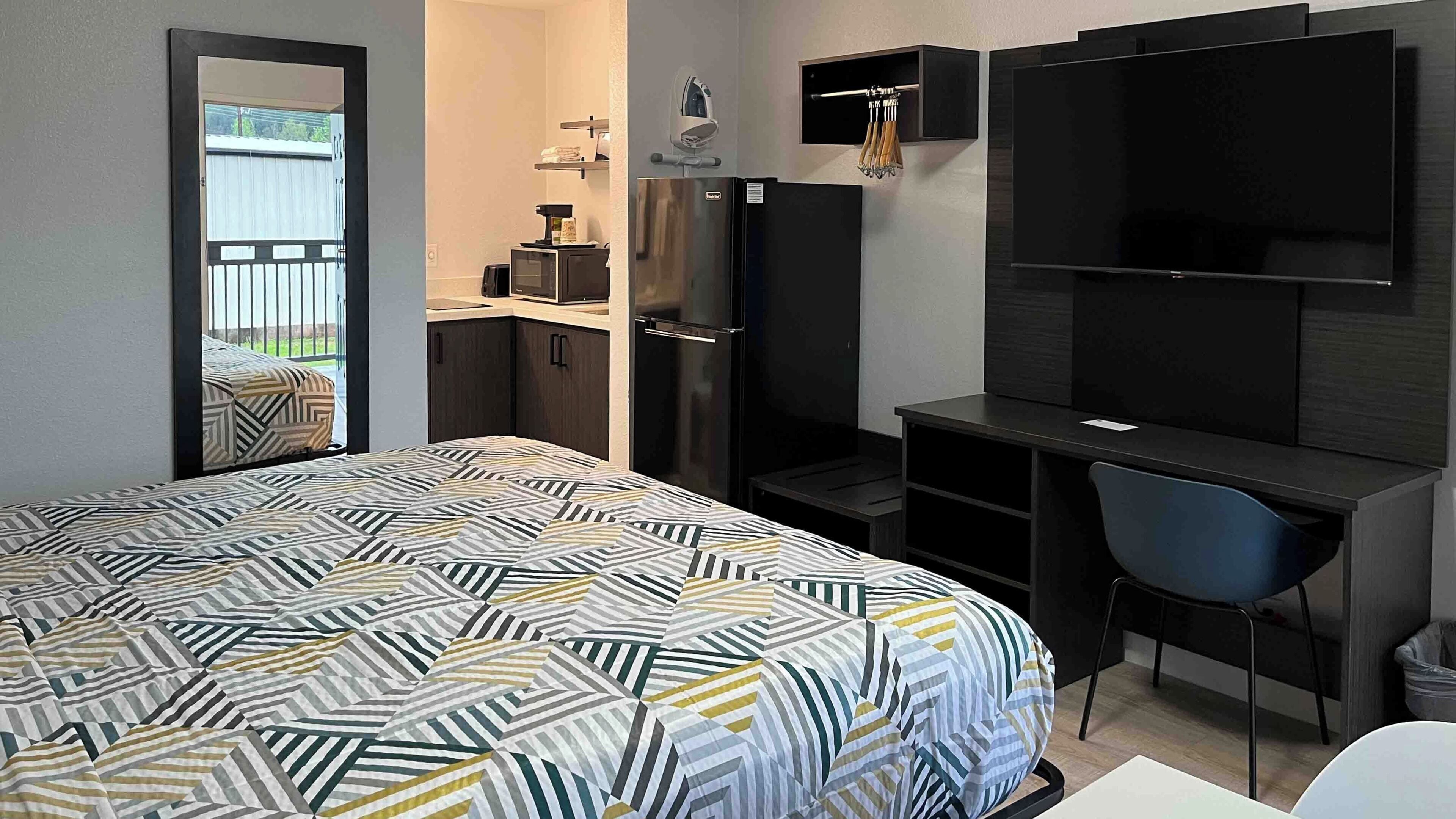 A bedroom with a bed, a desk, a chair, a TV, a wardrobe, and a mirror.