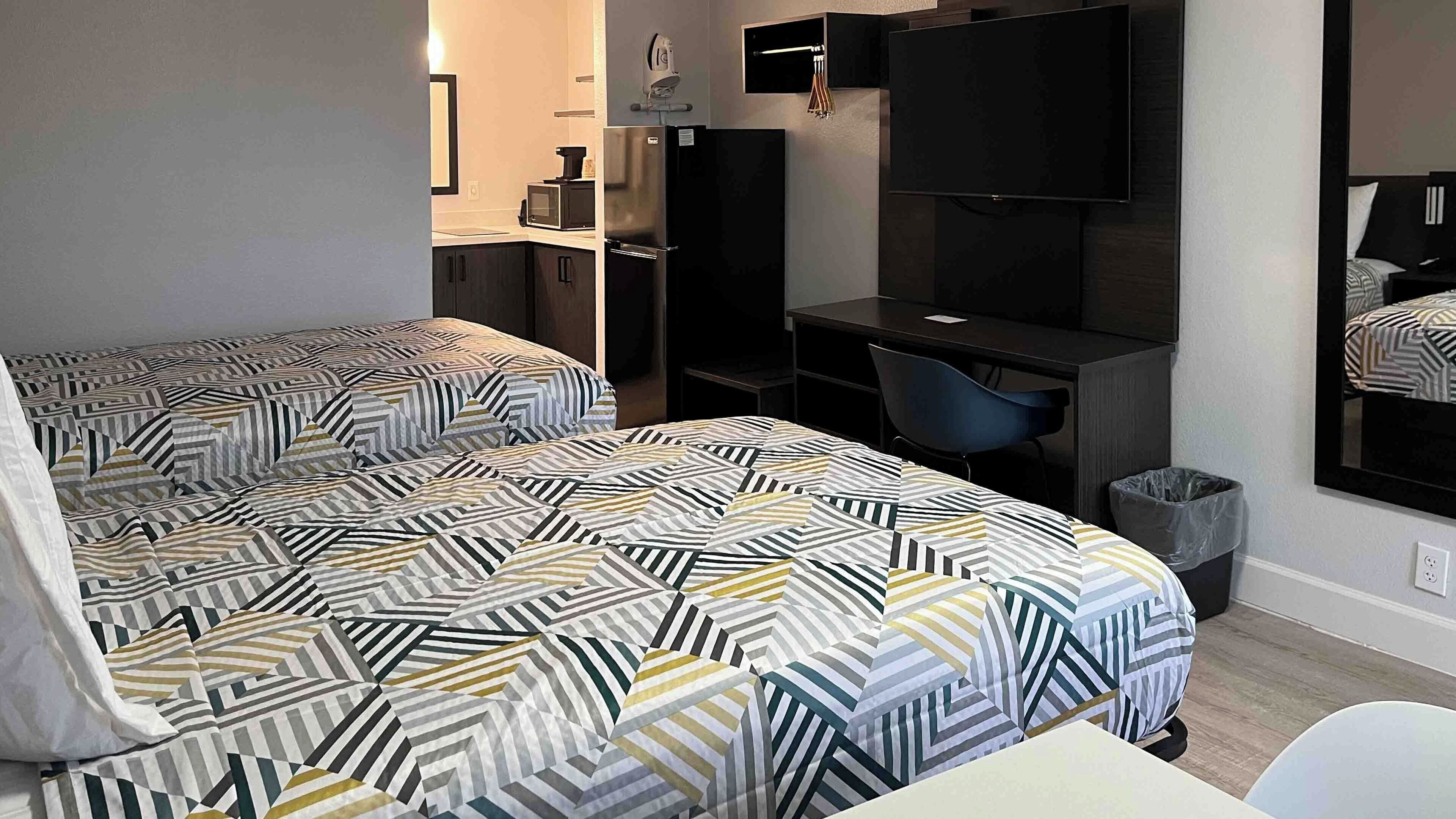 Habitación de hotel con dos camas, un escritorio, una silla, un televisor y un bote de basura pequeño.