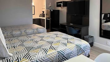 Habitación de hotel con dos camas, un escritorio, una silla, un televisor y un bote de basura pequeño.