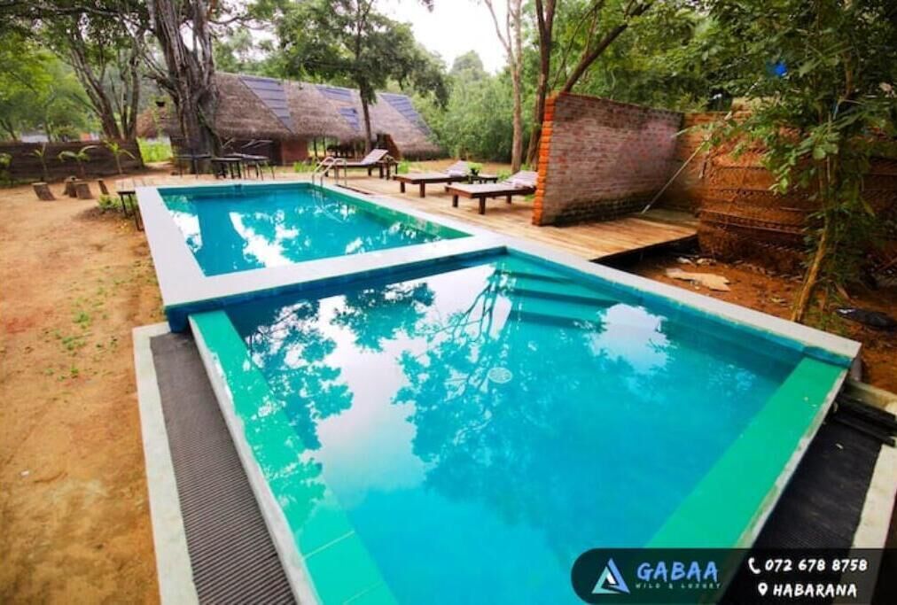 Ein Swimmingpool mit Holzterrasse und Liegestühlen, umgeben von Bäumen und einer Struktur mit Reetdach.