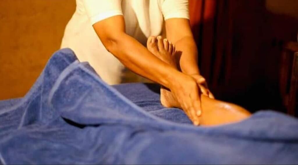 A massage therapy session with a person receiving a back massage on a bed covered with a blue sheet.