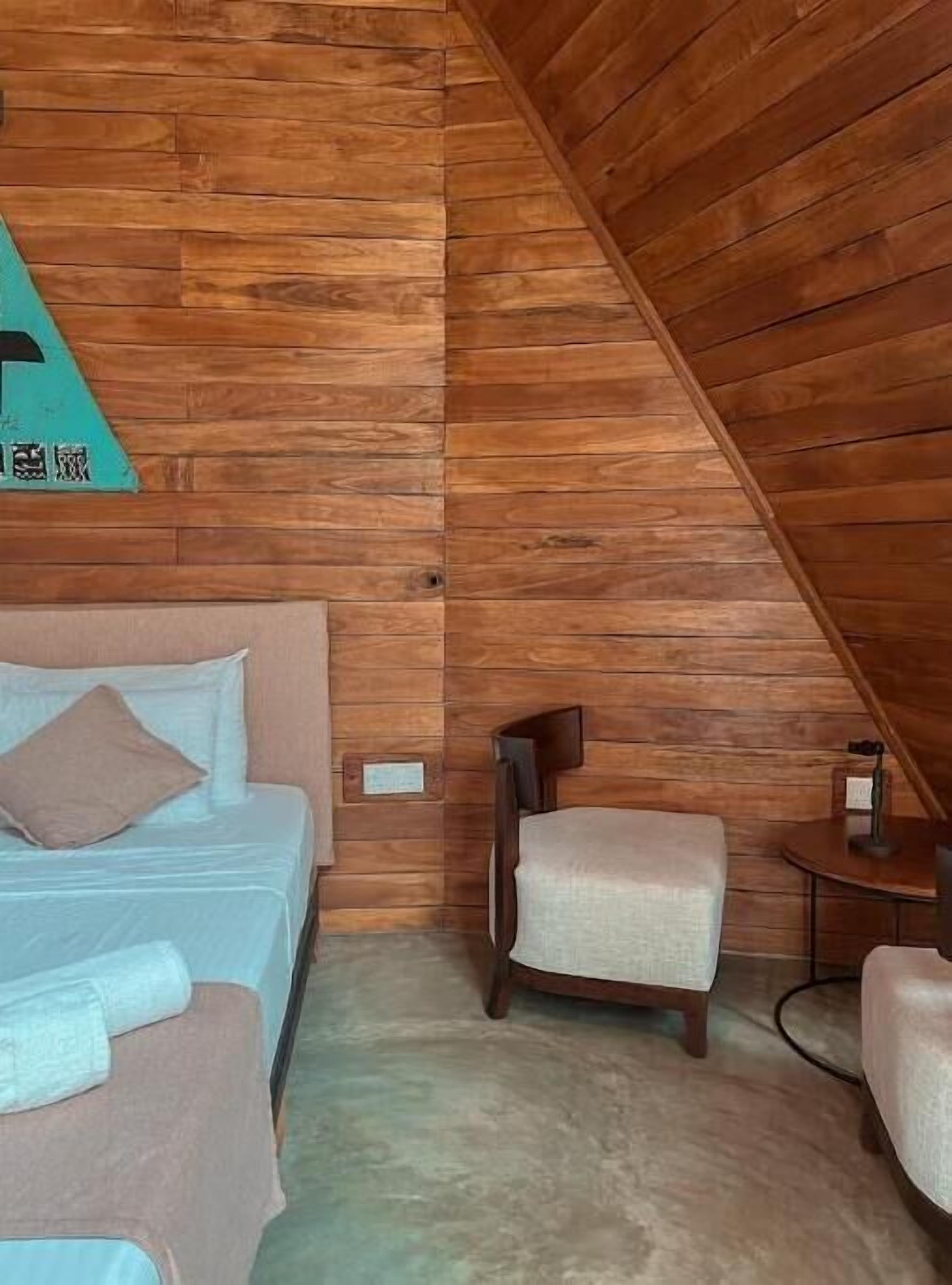 Una stanza accogliente con soffitto spiovente in legno, un letto con testiera beige, un piccolo tavolino rotondo e una sedia.