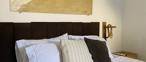 A neatly made bed with white and striped pillows, a textured white bedspread, and a large abstract painting above it.