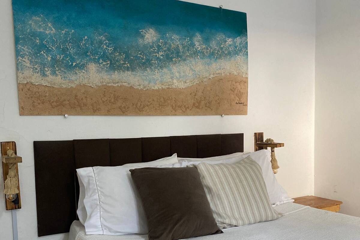 A bed with a white bedspread, a headboard, and a painting of a beach scene above it.