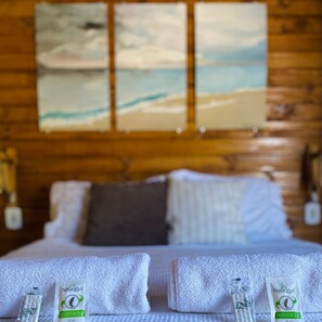 Une chambre d’hôtel avec une tête de lit en bois, un lit avec du linge de lit blanc, deux serviettes et deux bouteilles de shampoing.